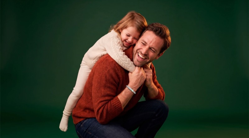 A father laughing with his daughter on his back, the Larkin band on his wrist