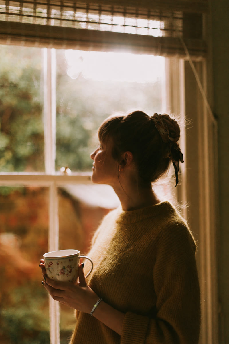A woman at a sunlit window holding a flowered mug, the white Larkin band on her wrist