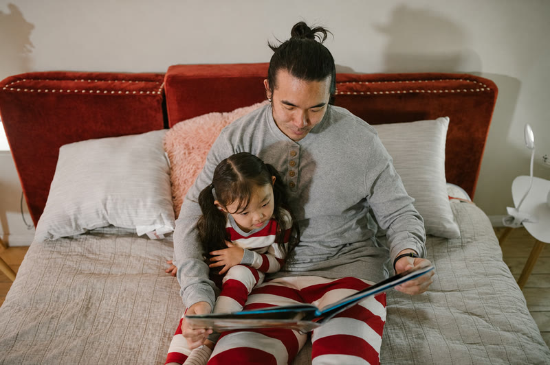 A father reading a picture book to his daughter on the bed, the black Larkin band on his wrist